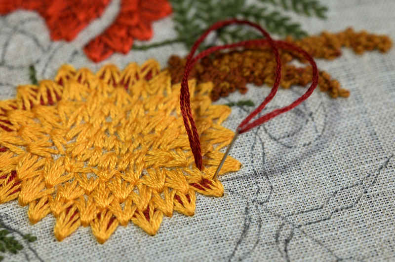 Close up view of yellow and burgundy chrysanthemum in progress. Some of the surrounding pattern is embroidered in rich fall colors, other areas are still unfinished.