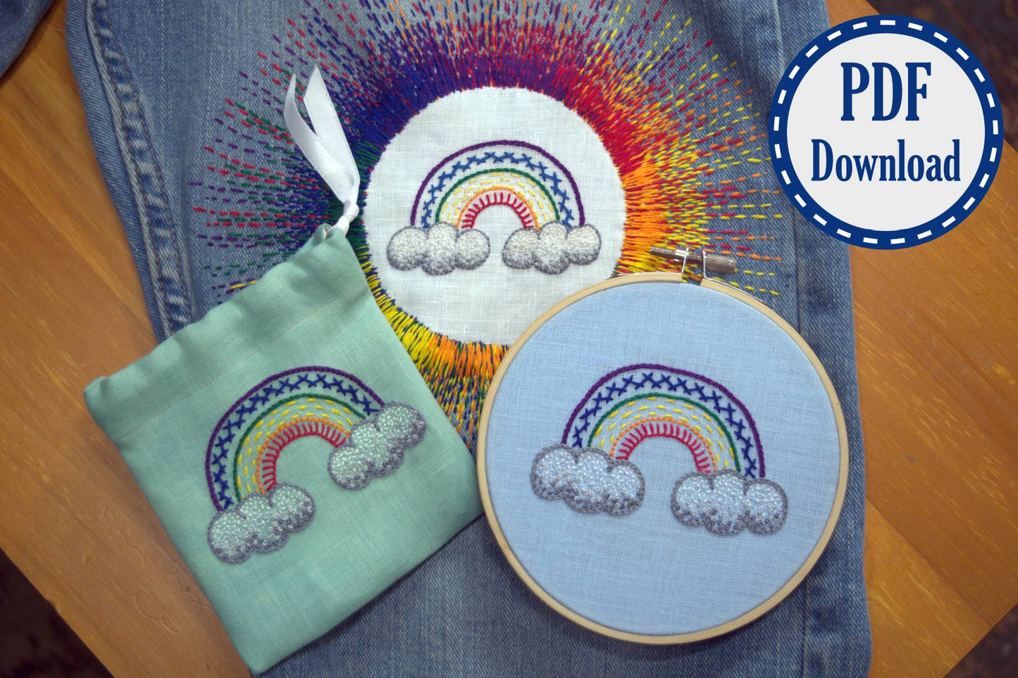 Three embroidered rainbows of the same design - one framed in hoop, one on small pouch, and one appliqued to a pair of jeans with sunburst of rainbow stitches