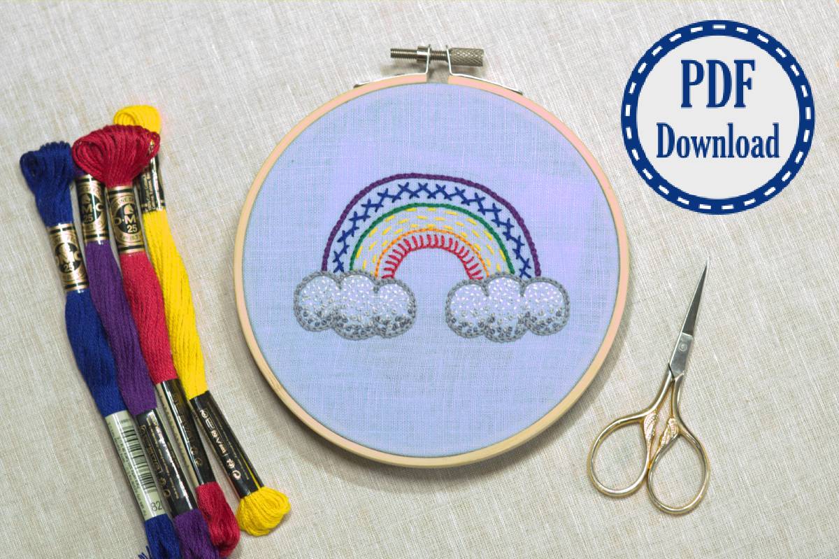 Embroidered rainbow in a variety of stitches framed in embroidery hoop with floss and scissors