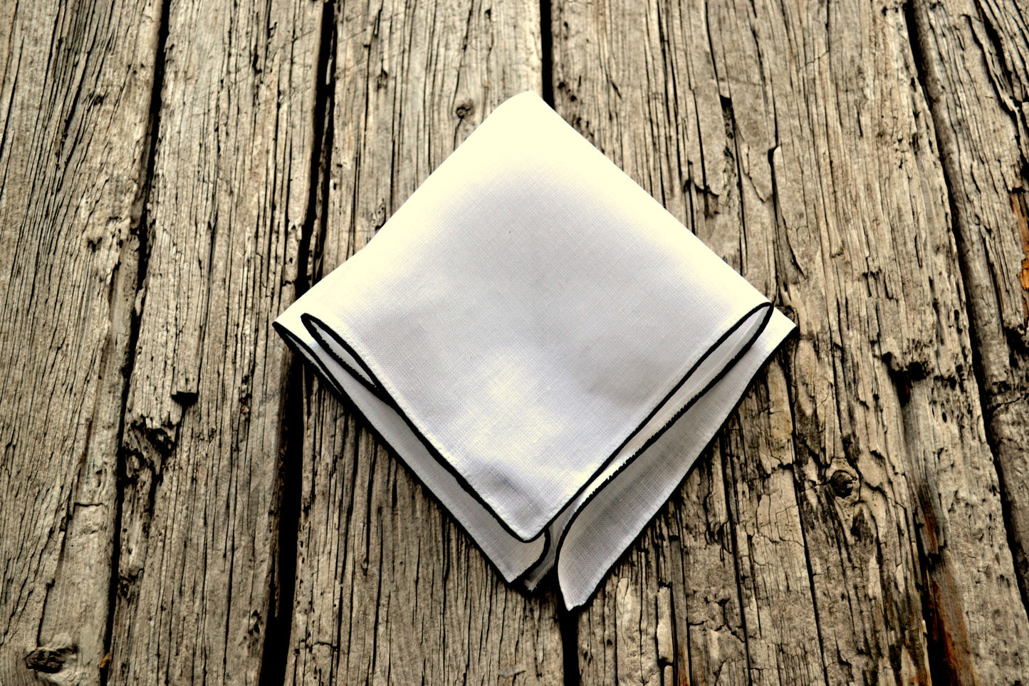 White linen handkerchief with black satin edge folded on wood background