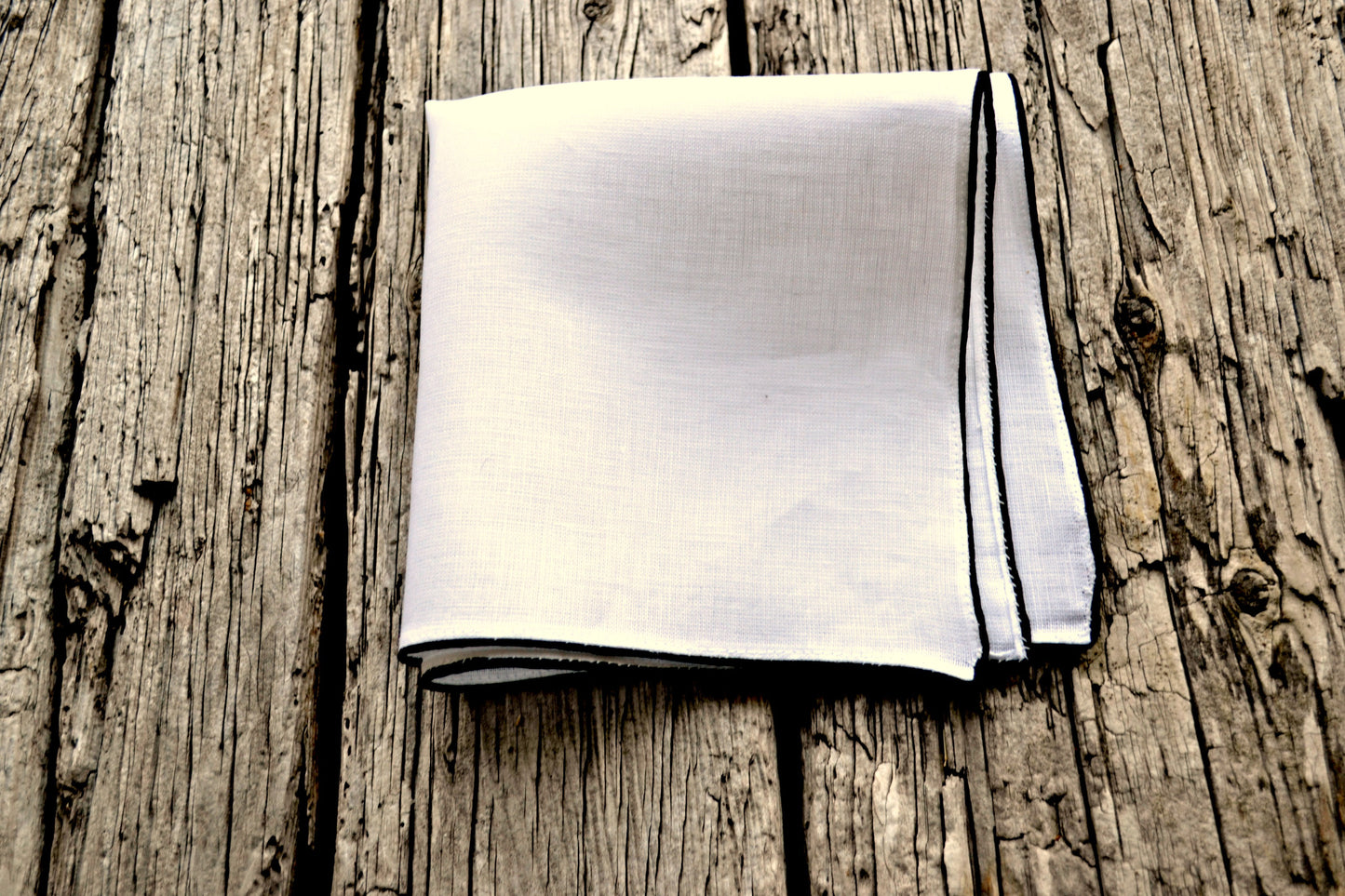 White Irish linen pocket square, folded in quarters, with black satin corded hem