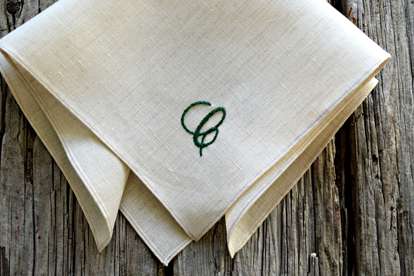 Closeup of natural colored linen pocket square with hand embroidered C in green, in cursive script