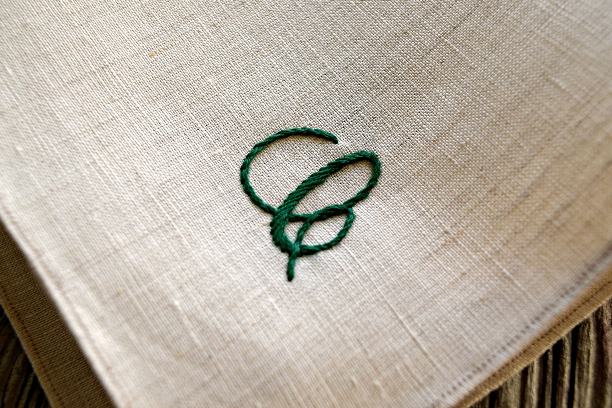 Closeup of oatmeal linen handkerchief showing hand embroidered letter C in cursive script