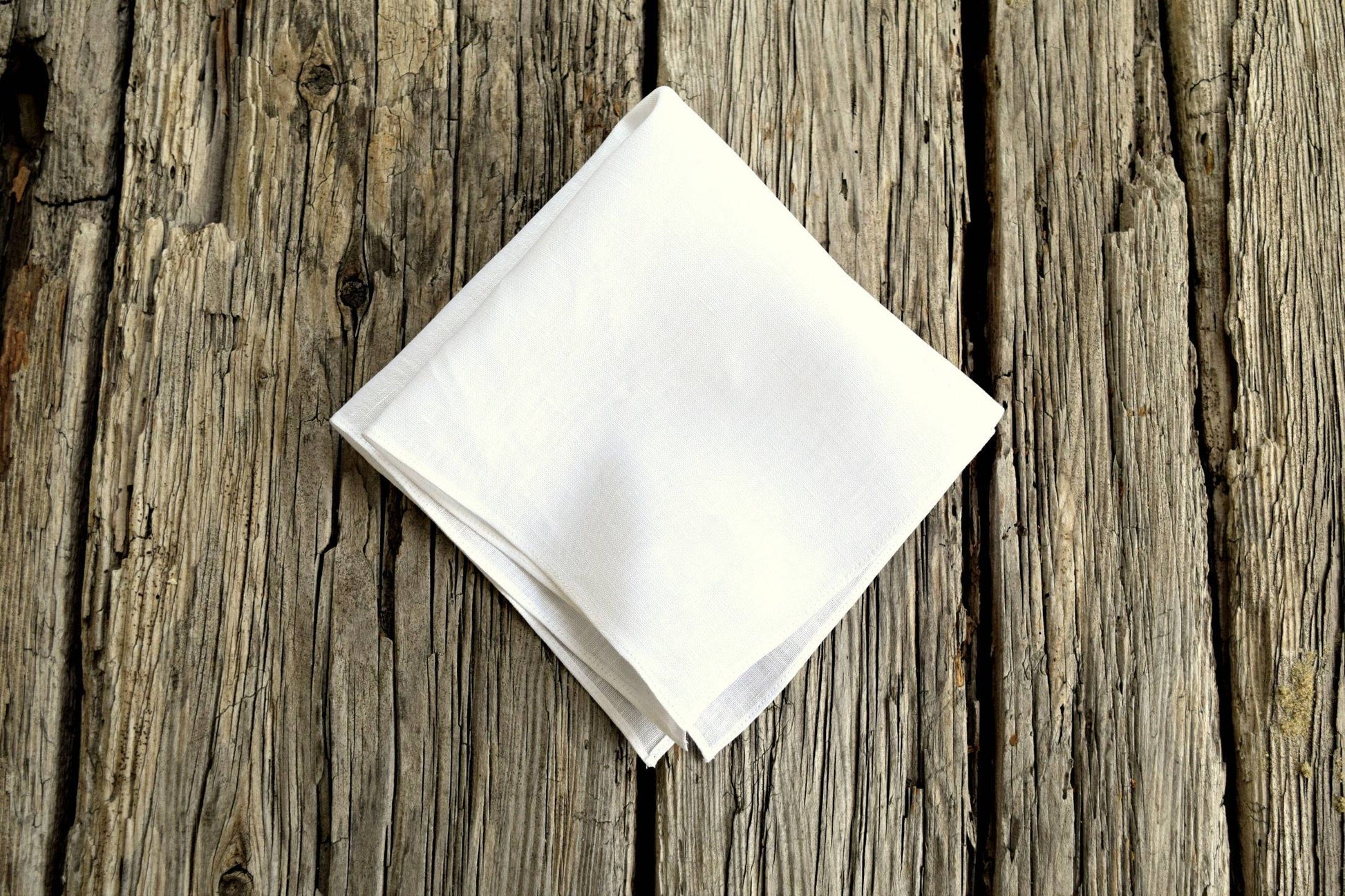 White Irish linen handkerchief folded into quarters and resting on weathered wood boards