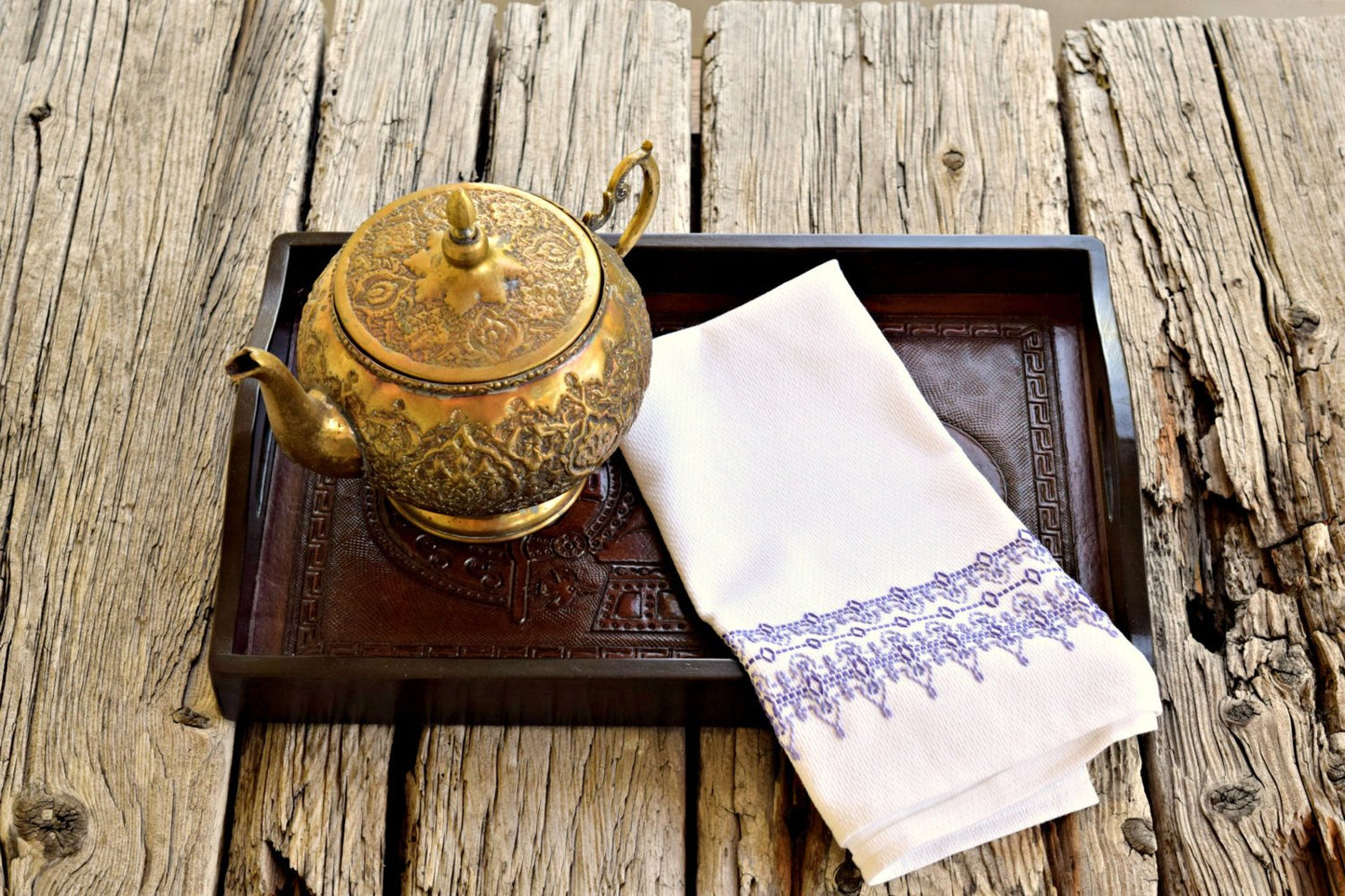 White huck kitchen towel embroidered with filigree design in shades of lavender on tray with Moroccan teapot