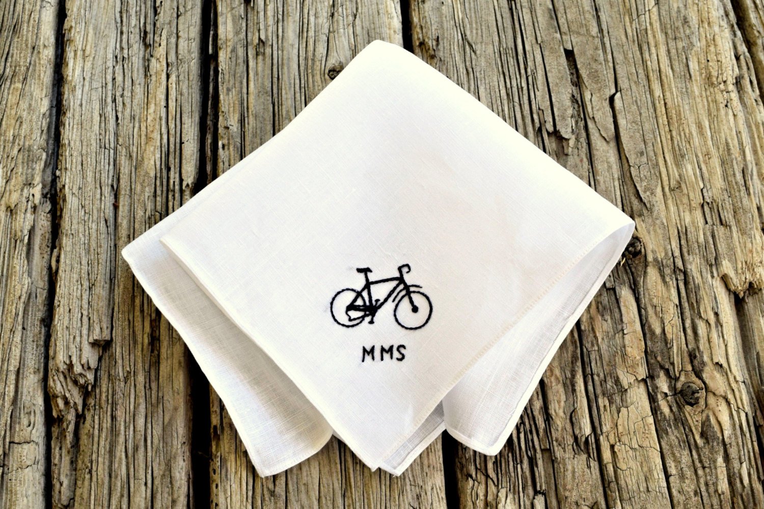 White linen handkerchief embroidered with small bicycle silhouette and the initials MMS in black