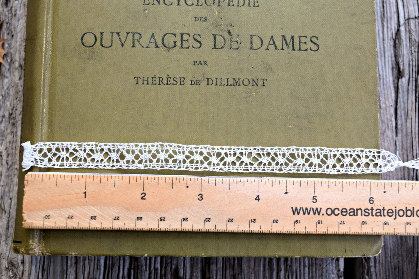 Handmade bobbin lace on book with ruler showing size - approximately three repeats per inch and half inch wide