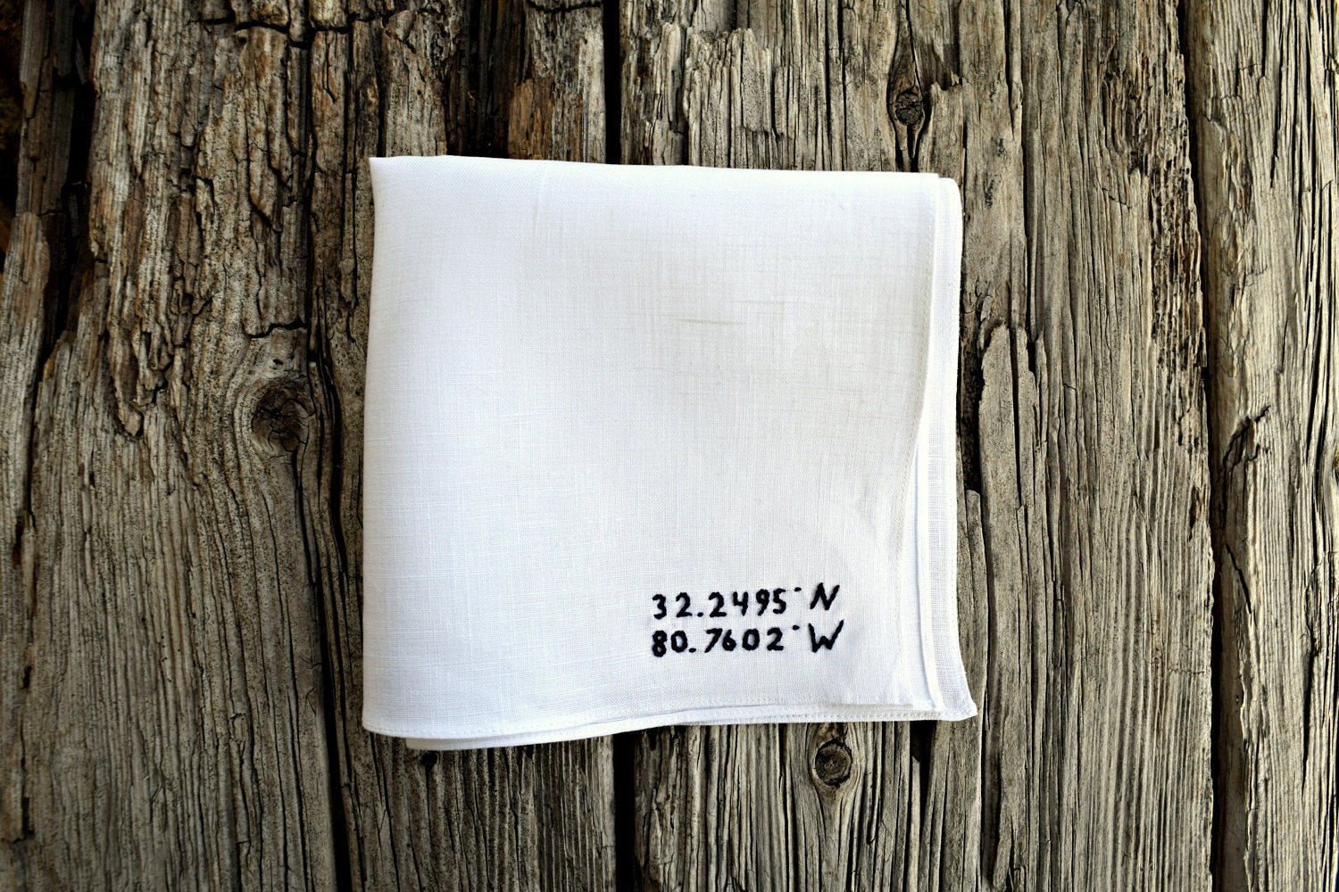 White linen handkerchief with GPS coordinates on wood background