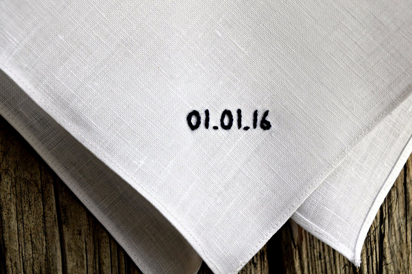 Closeup of white linen hand embroidered pocket square with wedding date detail