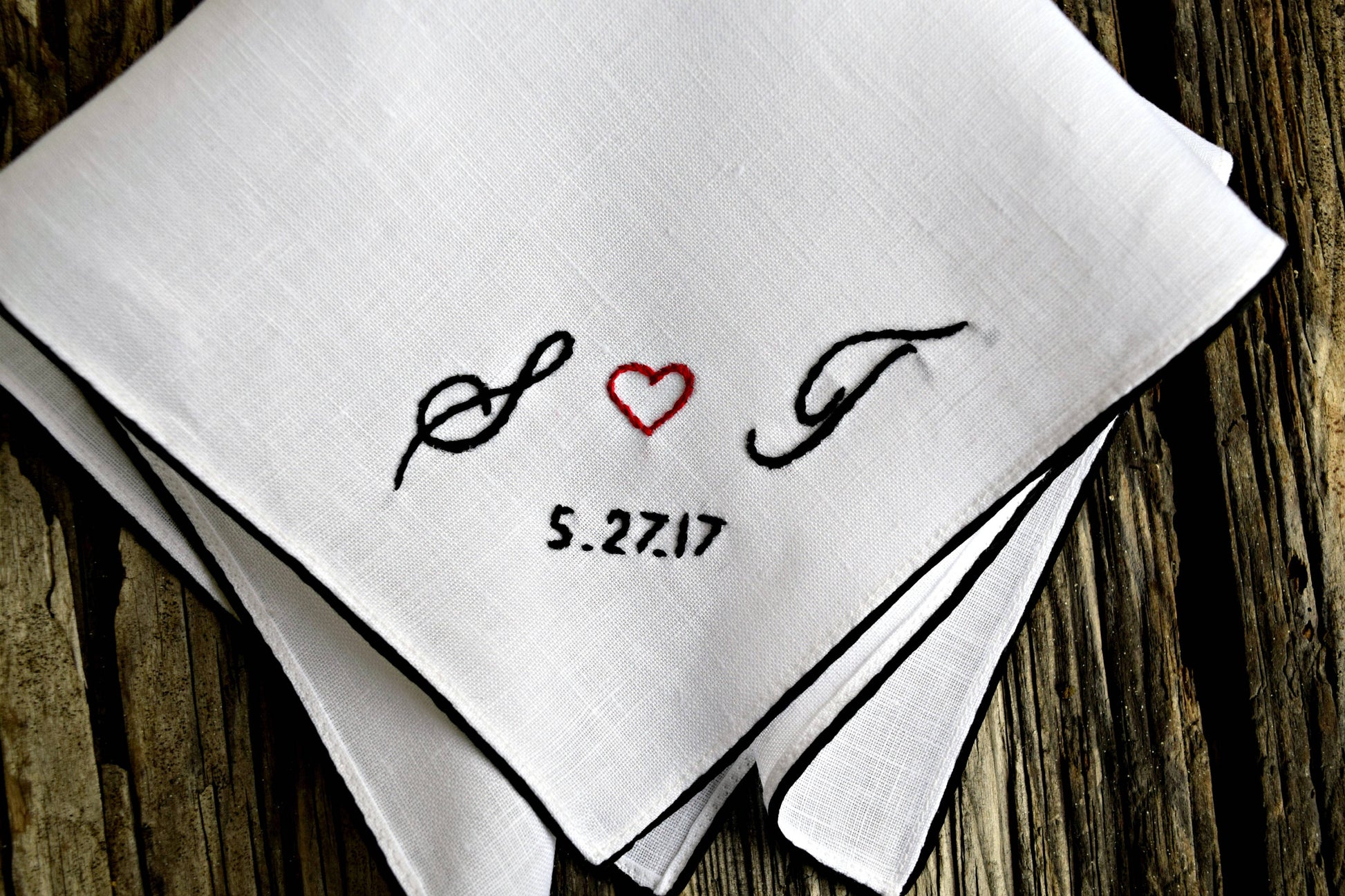 Closeup of white Irish linen handkerchief with color border, with hand embroidery that reads S heart T 5.27.17 in cursive script, lettering black with red heart