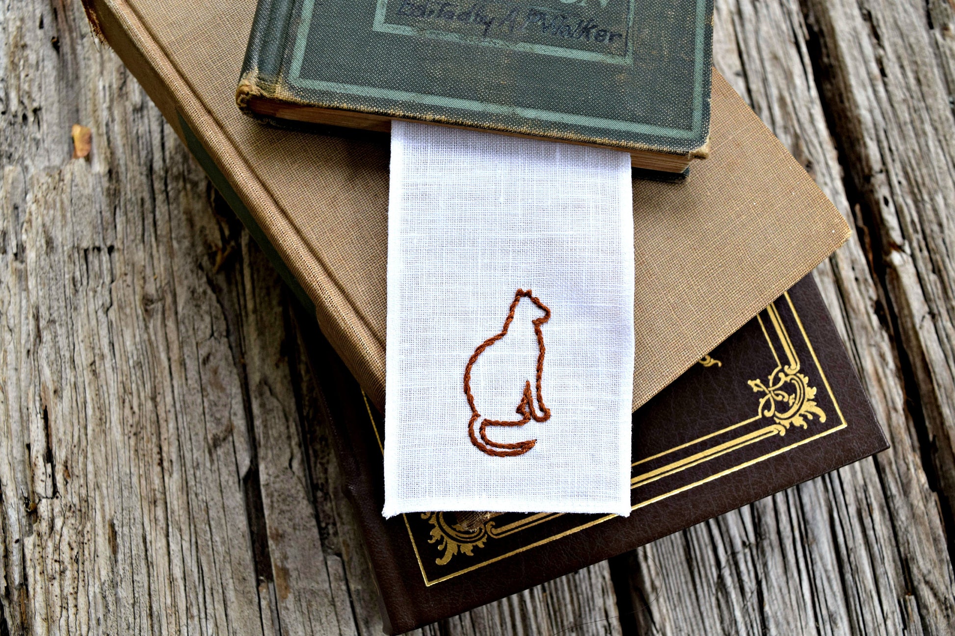 Hand embroidered bookmark with cat silhouette in a pile of books
