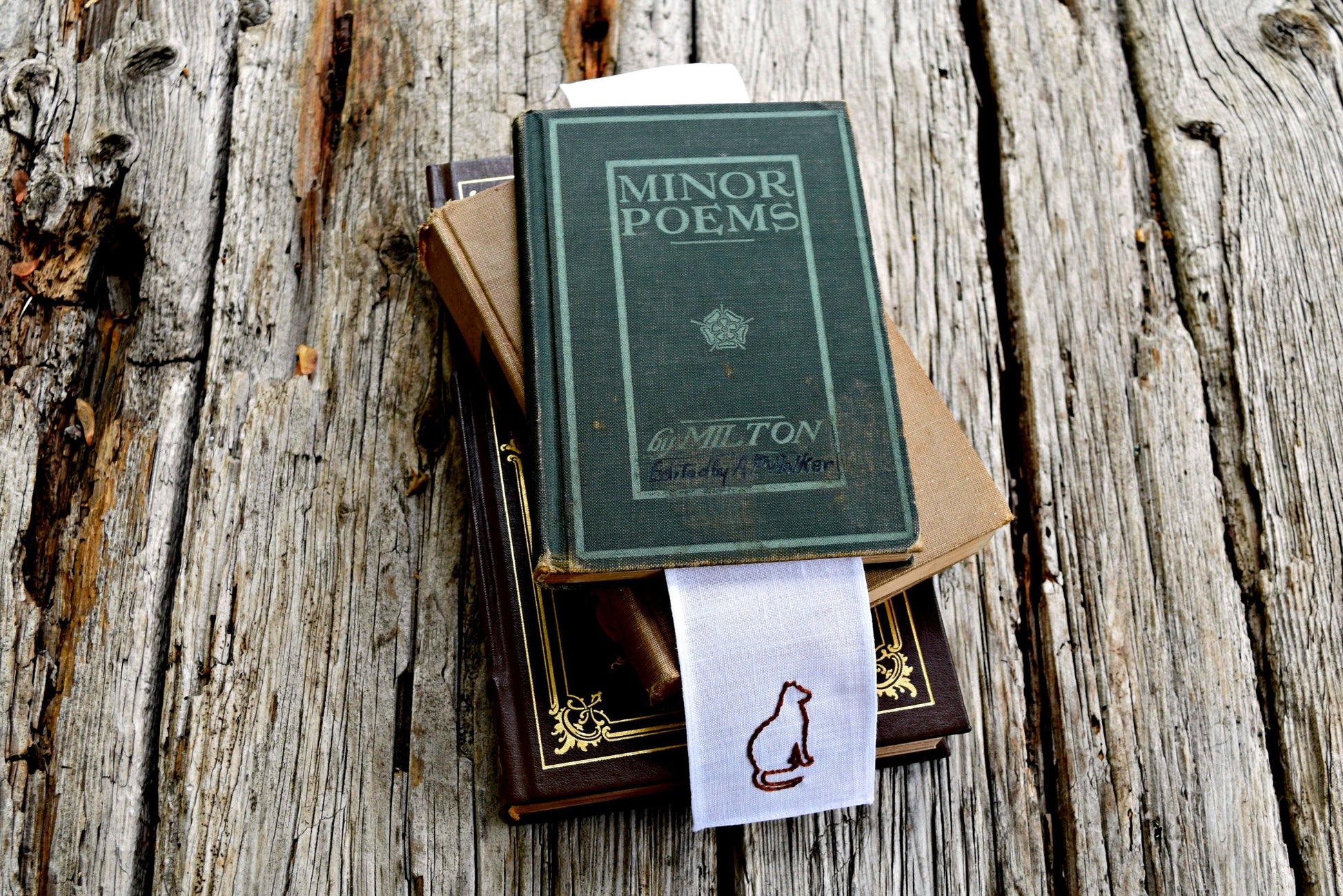 Hand embroidered cat silhouette on a bookmark in pile of vintage books