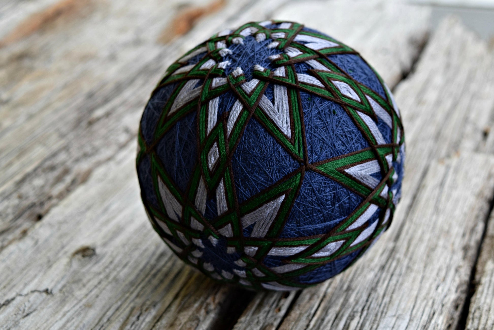 Close up of navy temari ball with hand embroidered grey, green, and brown stars