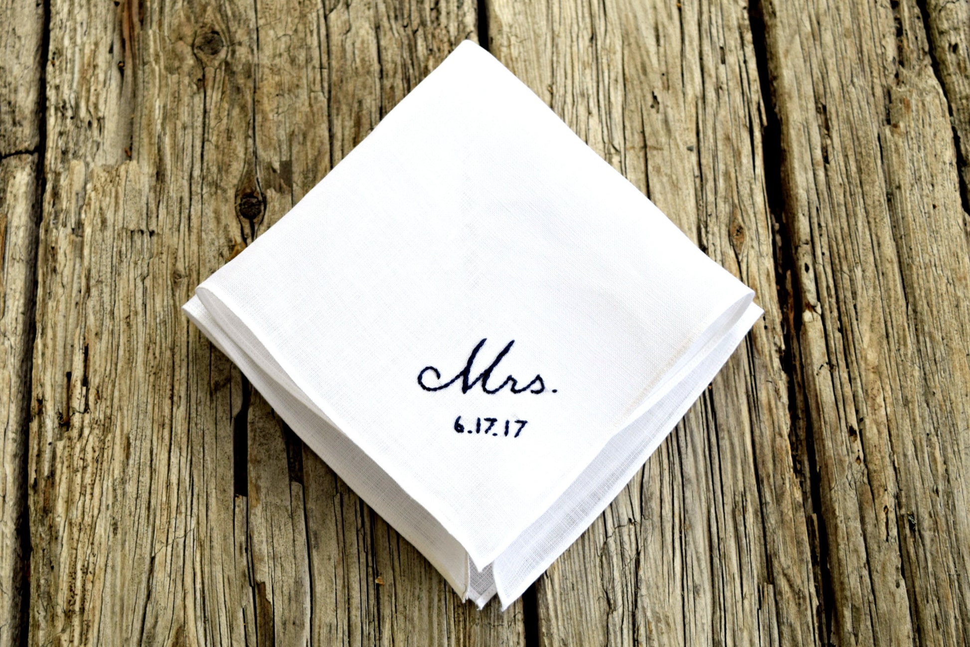White linen handkerchief embroidered with Mrs. 6.17.17 in black on wood background