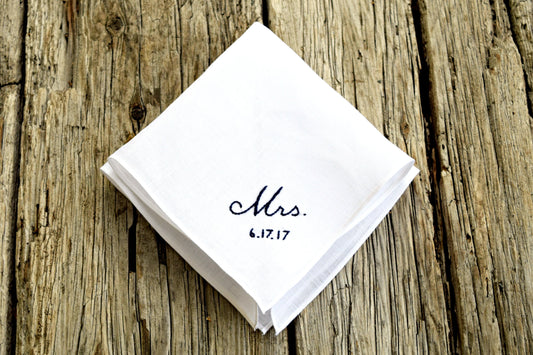 White linen handkerchief embroidered with Mrs. 6.17.17 in black on wood background