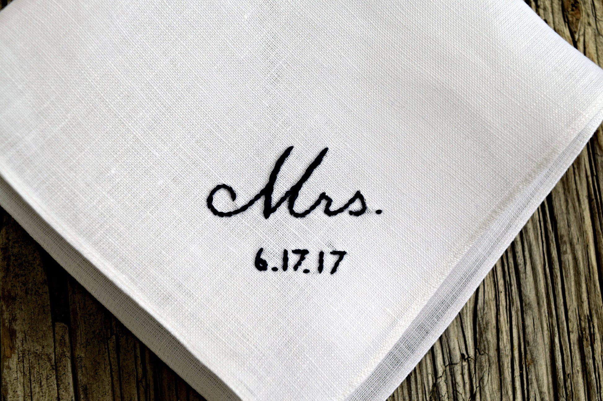 Closeup of white linen hankie embroidered with Mrs. and wedding date in black hand embroidery