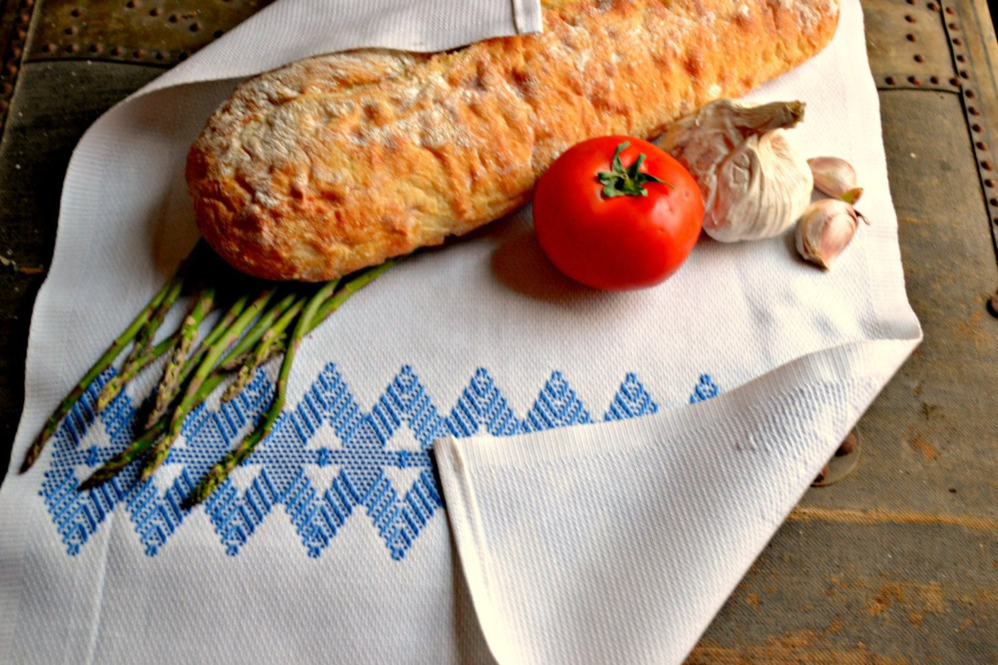 White tea towel embroidered in blue showing back of work as well as bread and veggies