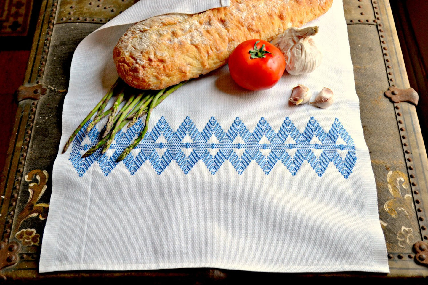 Tea towel hand embroidered with traditional diamond pattern in blue wrapping produce and bread
