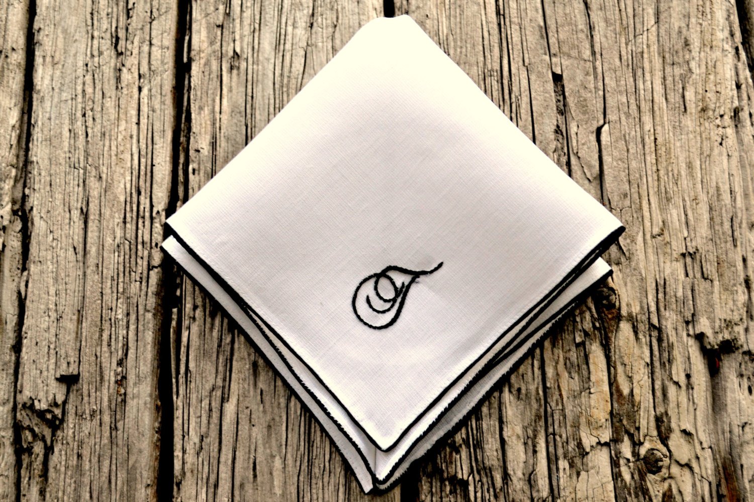 White linen handkerchief with satin border and script letter T in black