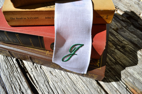 Hand embroidered white linen bookmark with script initial in stack of books