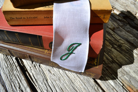 Hand embroidered white linen bookmark with script initial in stack of books