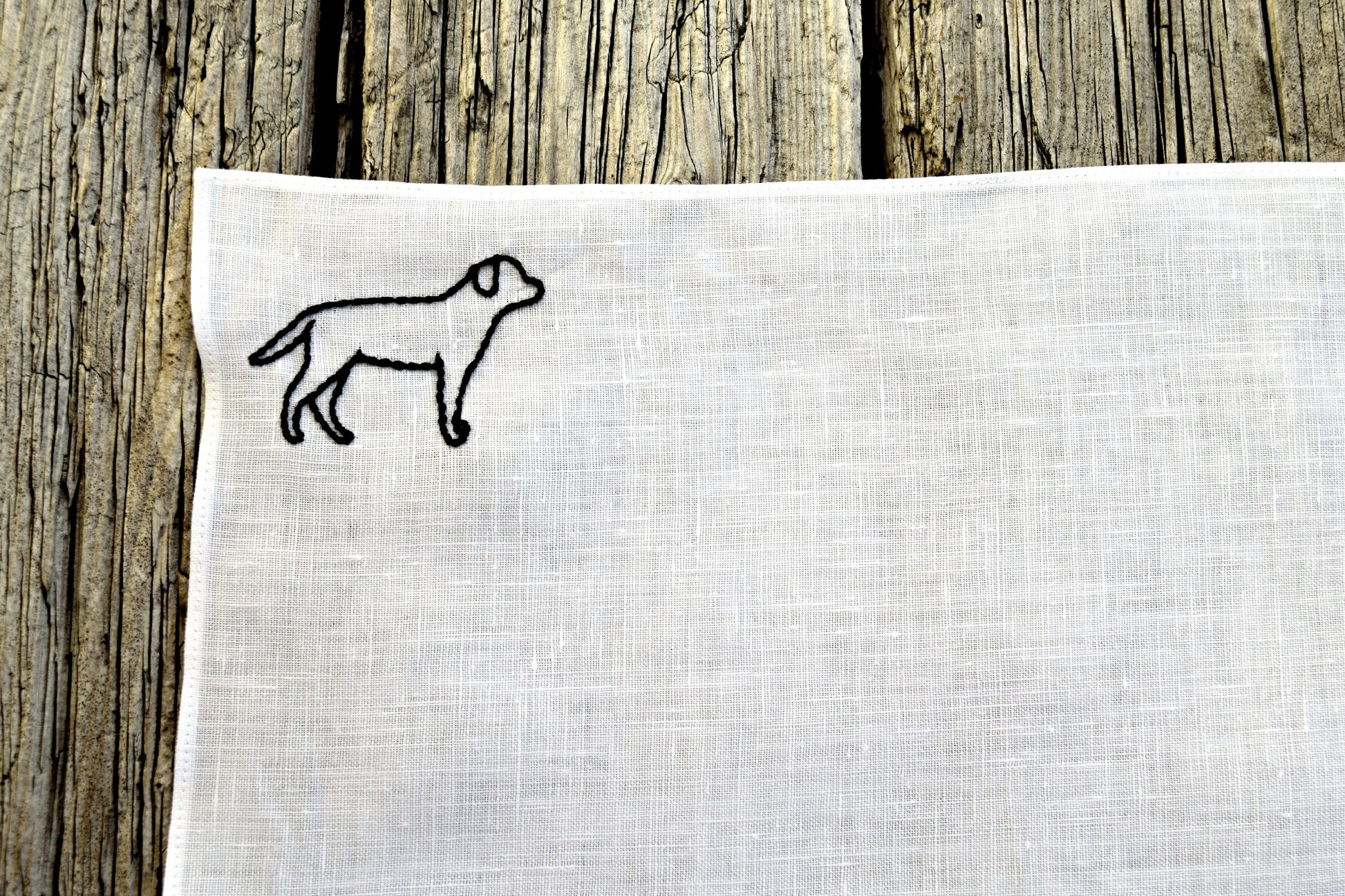 Corner of white linen handkerchief hand embroidered with a black labrador silhouette