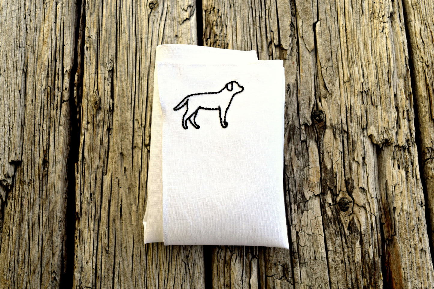 Folded white linen handkerchief embroidered with an outline of a black labrador retriever in one corner