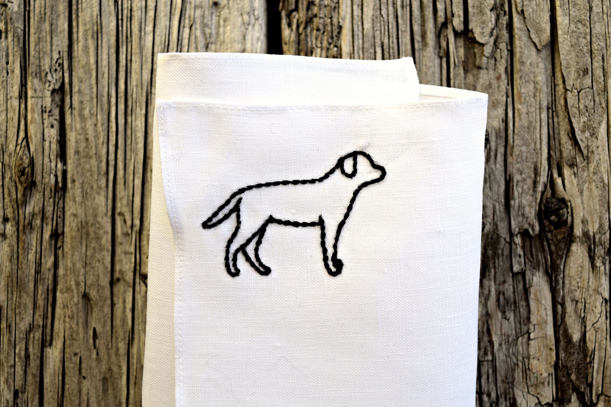 Folded white Irish linen pocket square hand embroidered with the outline of a black lab