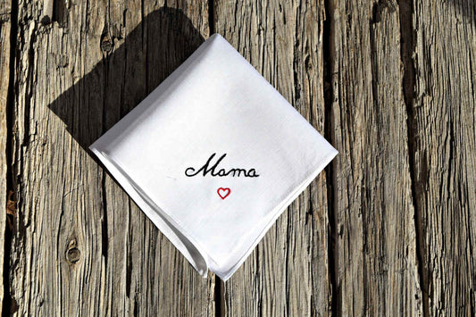 White linen handkerchief folded, hand embroidered with "Mama" in black and a small red heart below