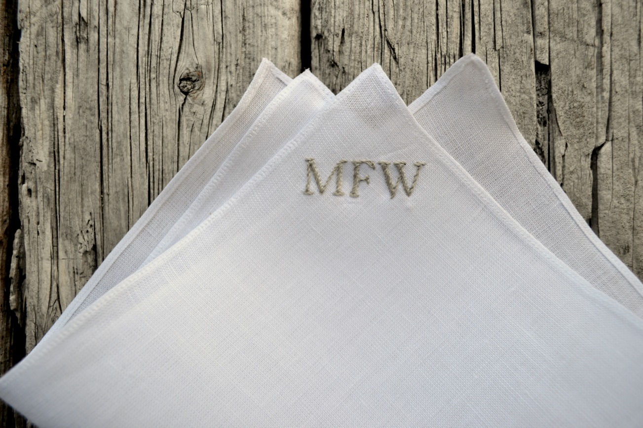 White Irish linen pocket square closeup showing letters in a color matched to faded barn boards in the background
