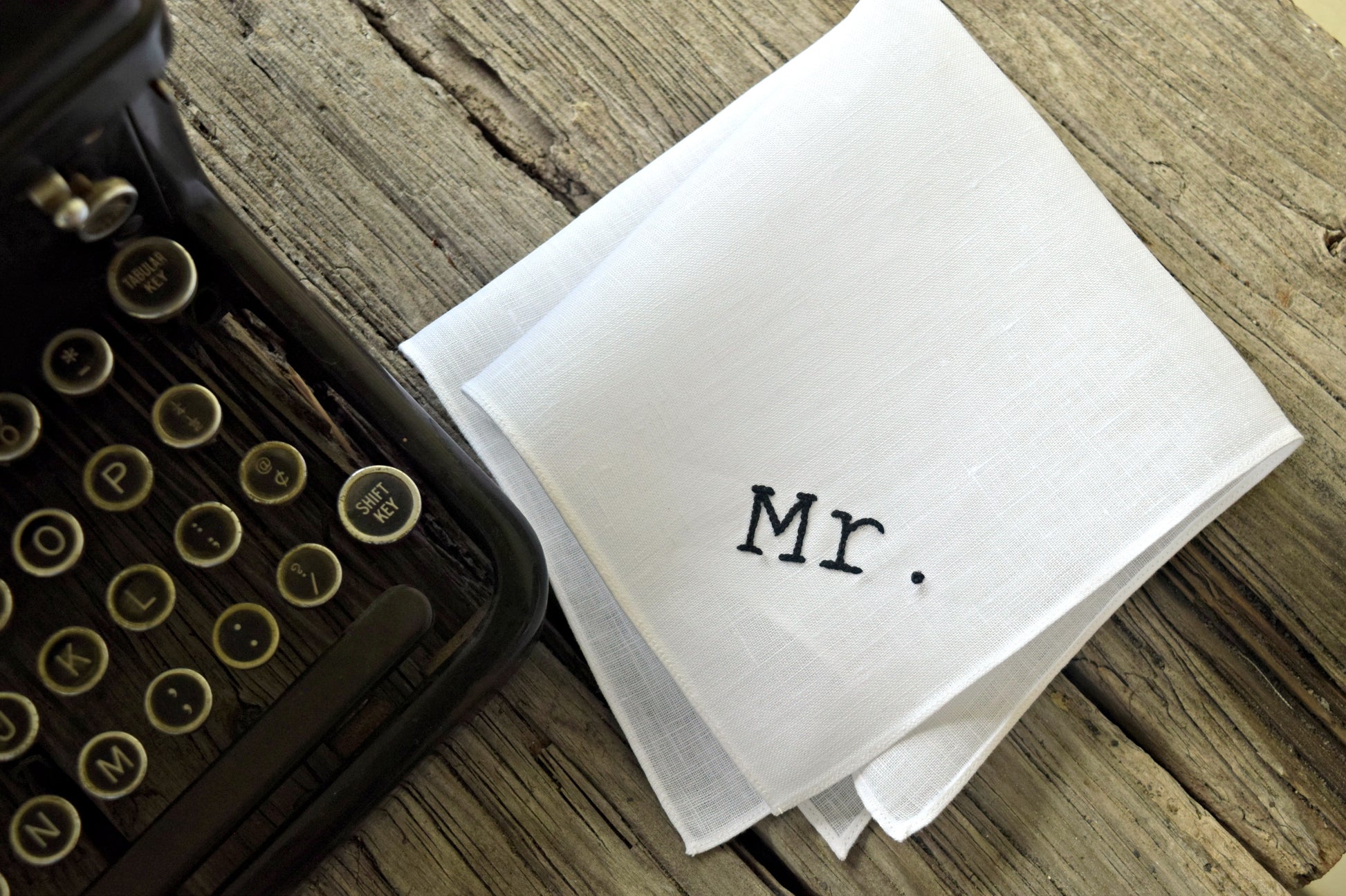 White linen pocket square hand embroidered with Mr. in typewriter script next to old typewriter