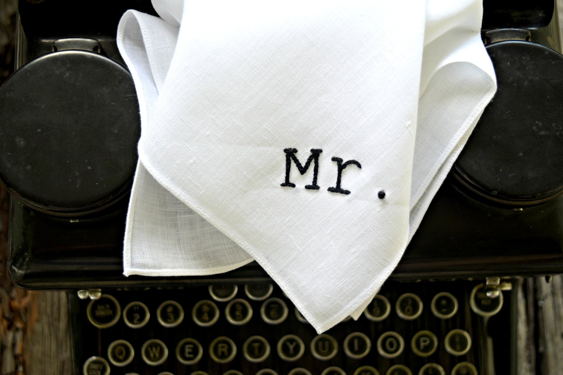Closeup of white linen hankie hand embroidered with the word Mr.  on a typewriter