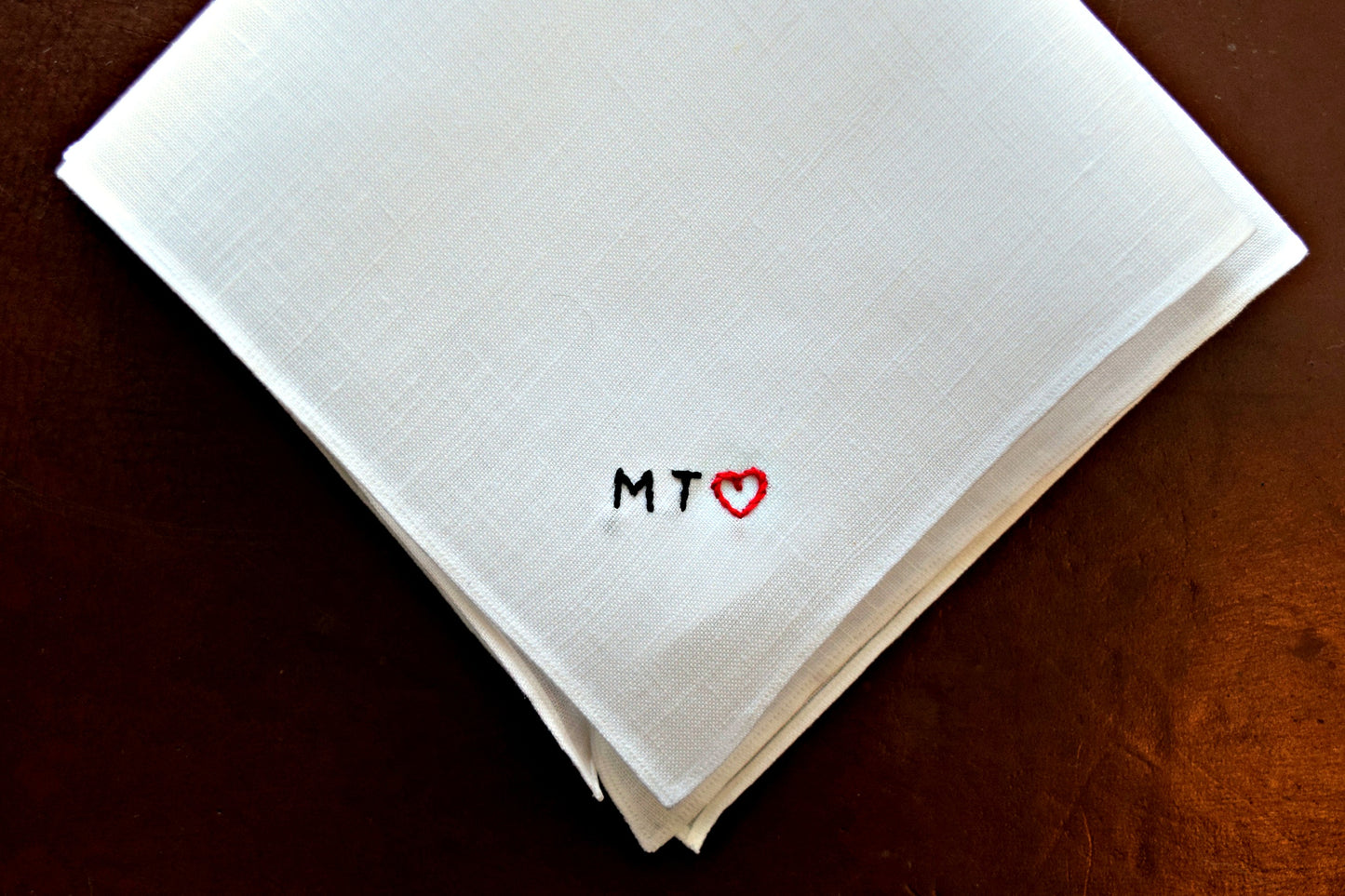 Close up of white pocket square embroidered with small black initials and red heart