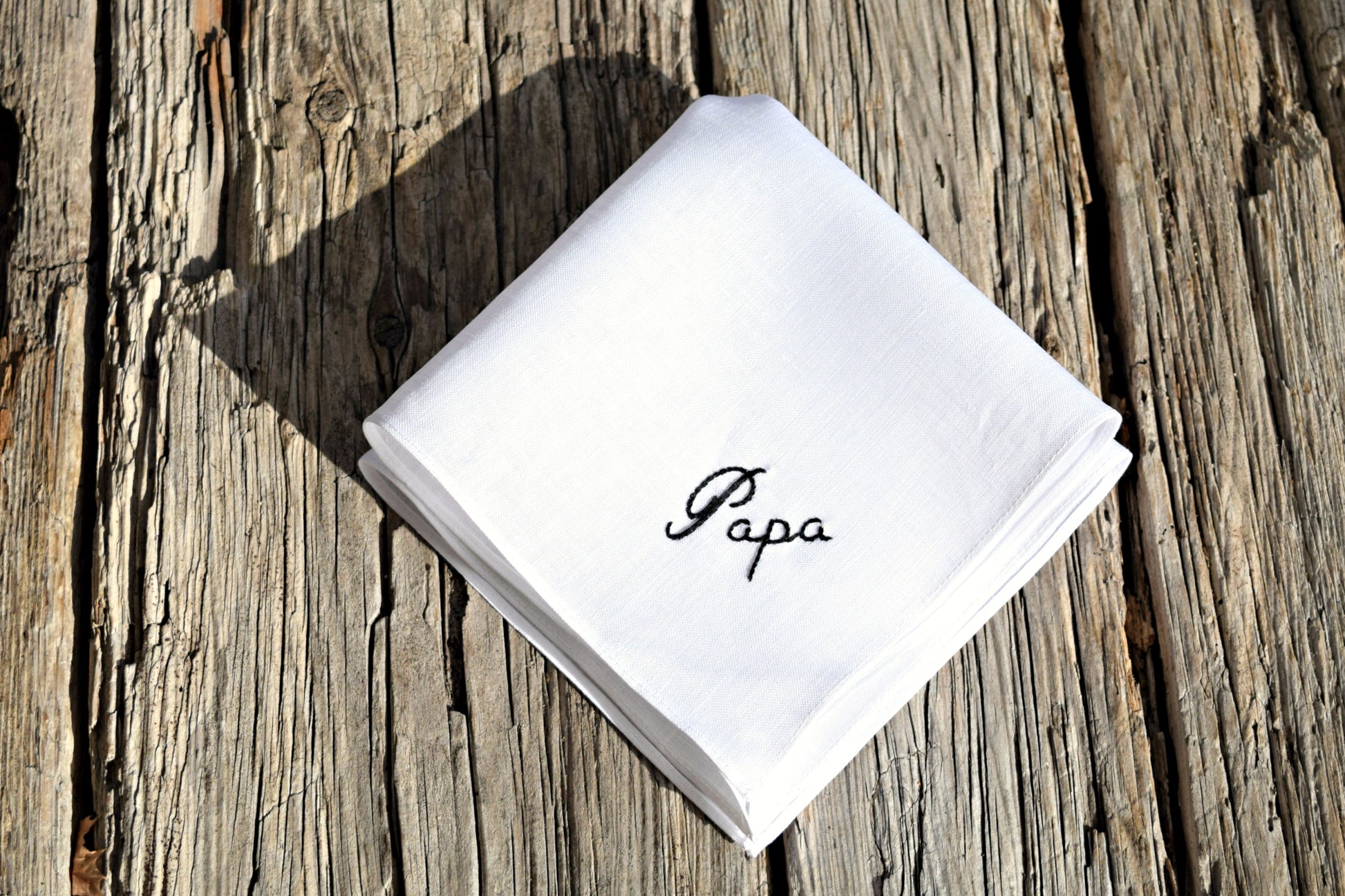 White Irish linen handkerchief embroidered with 'Papa' on a wood background